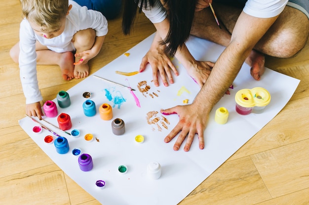 Foto feliz hijo de la familia con los padres y un gato pintando un cartel y el otro con pinturas