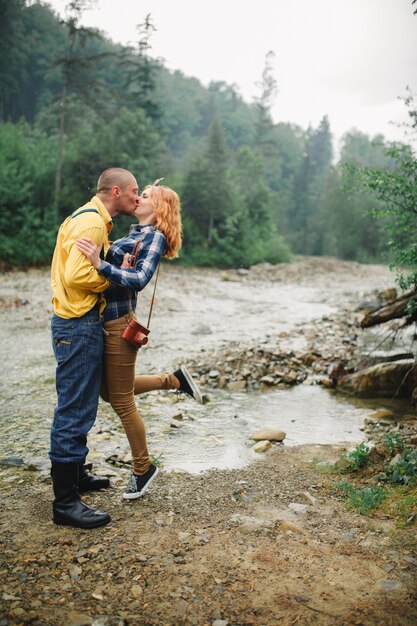 Feliz hipster pareja besándose y abrazándose cerca del río en la montaña. Pareja de turistas