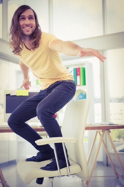 Feliz hipster de pie en la silla de escritorio en la oficina