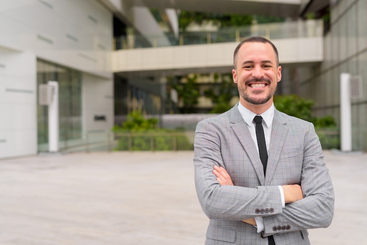 Foto feliz hispano empresario calvo barbudo sonriendo con los brazos cruzados en el exterior de la ciudad