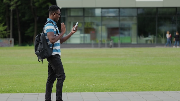 Feliz hombre africano hablando de videollamada con un amigo en línea en el teléfono móvil en la calle urbana
