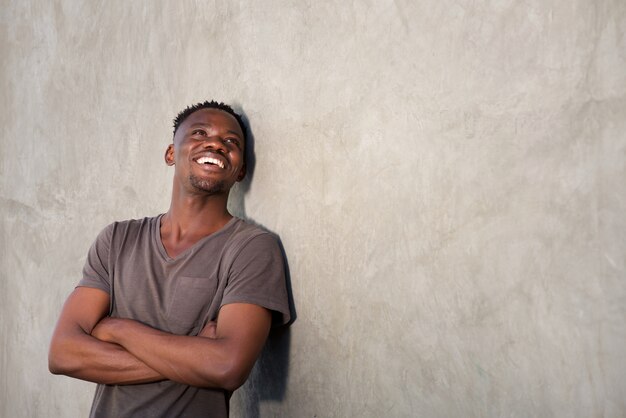 Feliz hombre africano sonriendo por la pared y mirando el espacio de la copia