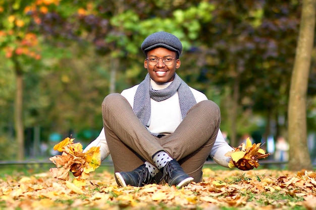 Feliz hombre afroamericano de etnia negra divirtiéndose en el parque de otoño dorado con hojas coloridas