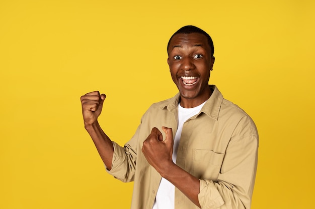 Feliz hombre afroamericano milenario casual con la boca abierta levanta los puños grita celebra