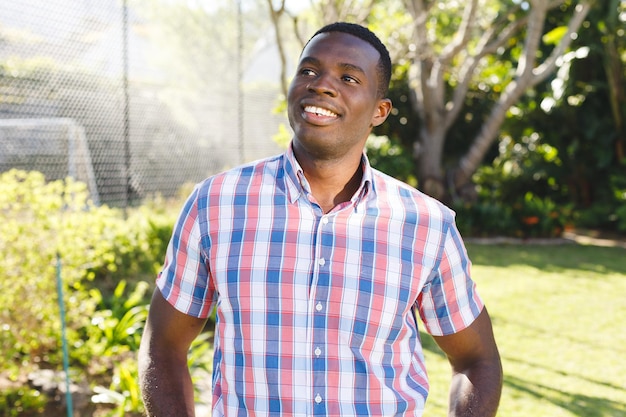 Feliz hombre afroamericano de pie en el soleado jardín sonriendo. Concepto de felicidad, salud, vida doméstica e inclusión.