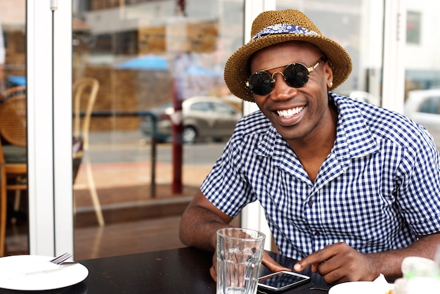 Feliz hombre afroamericano sentado en la cafetería con teléfono móvil