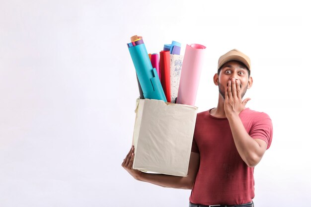 Feliz hombre asiático en camiseta y gorra con caja de papel de color aislada sobre fondo blanco, concepto de servicio de entrega