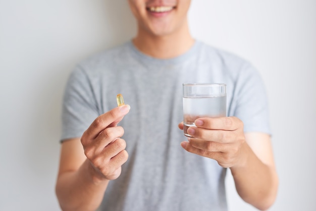 Feliz hombre asiático con píldora de vitamina omega 3 en casa