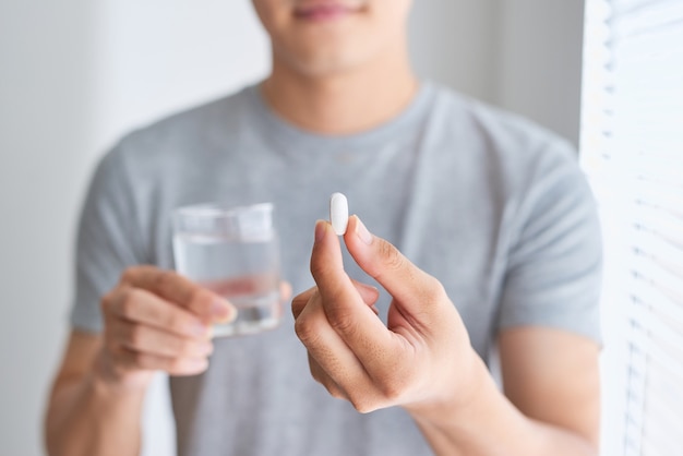 Feliz hombre asiático sosteniendo una pastilla y un vaso de agua mirando a la cámara