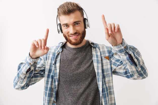 Feliz hombre barbudo en camisa y auriculares escuchando música