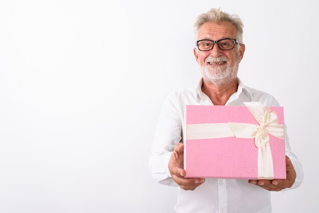 Feliz hombre barbudo senior sonriendo y dando caja de regalo mientras usa anteojos en blanco