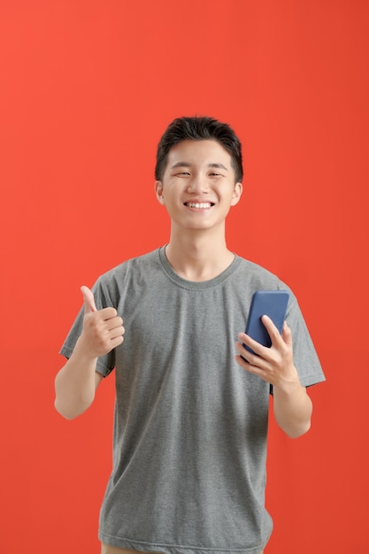 Feliz hombre casual sosteniendo smartphone y mostrando el pulgar hacia arriba sobre fondo rojo.