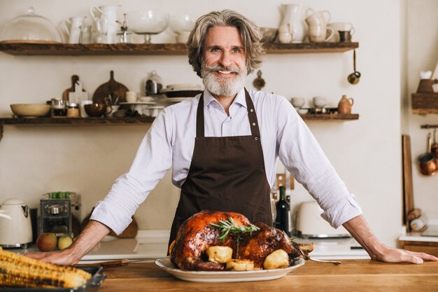 Feliz hombre maduro de pie en la mesa de Navidad con sabroso pavo asado