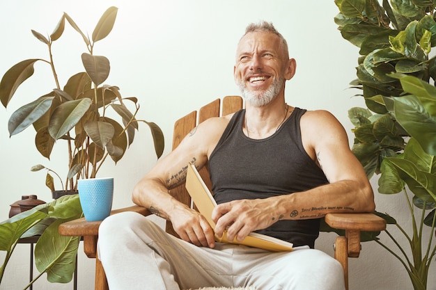 Feliz hombre de mediana edad con ropa casual sentado en la soleada terraza de su moderno apartamento
