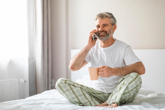 Feliz hombre de mediana edad sentado en la cama hablando por teléfono