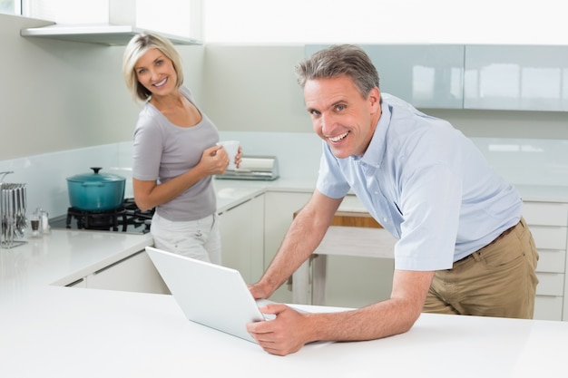 Feliz hombre y mujer con computadora portátil en la cocina