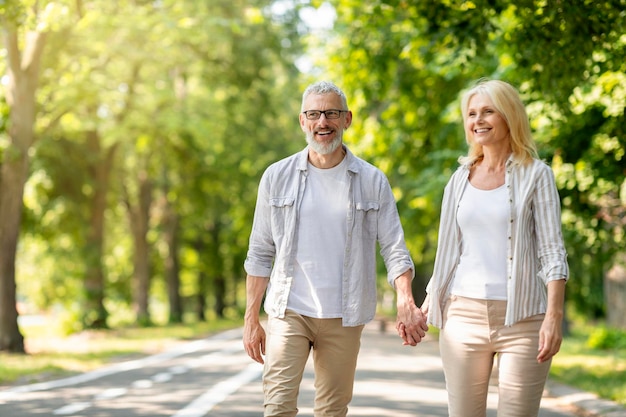 Feliz hombre y mujer maduros tomados de la mano y caminando juntos en el parque