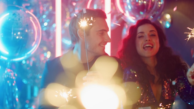 Feliz hombre y mujer sosteniendo destellos en el club Pareja bailando con luces de bengala