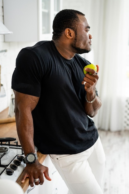 Feliz hombre multirracial está comiendo manzana en la cocina moderna Estilo de vida vegano y vegetariano Comida para adelgazar y comida saludable en el concepto de hogar