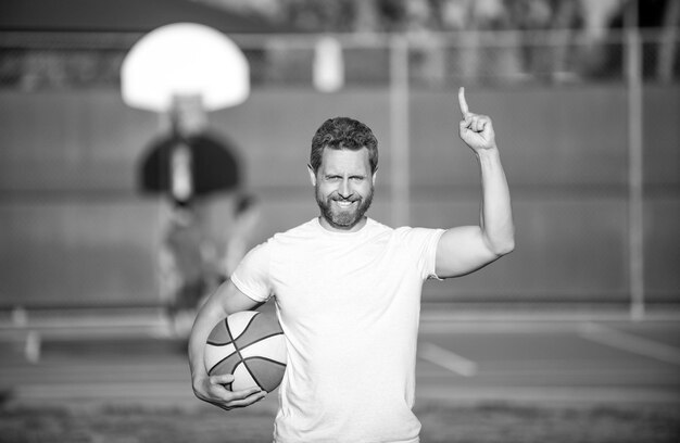 Feliz hombre musculoso deportista jugador de baloncesto levantado dedo sostener pelota deporte al aire libre