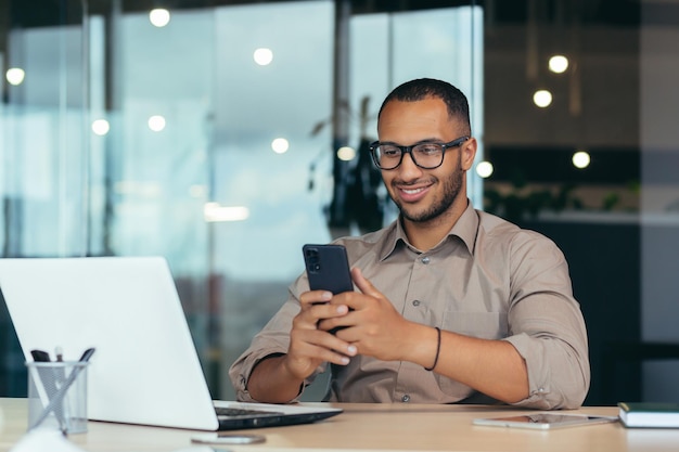 Feliz hombre de negocios afroamericano con gafas trabajando dentro de una oficina moderna con un hombre portátil con camisa