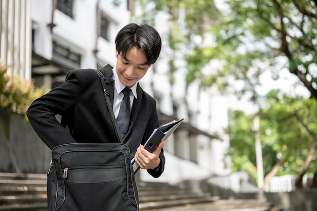 Un feliz hombre de negocios asiático encuentra su teléfono en su maletín mientras baja las escaleras