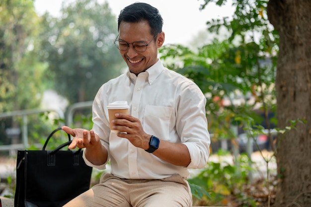 Foto un feliz hombre de negocios asiático se sienta al aire libre disfrutando de una pausa para un café en el parque público en un día brillante