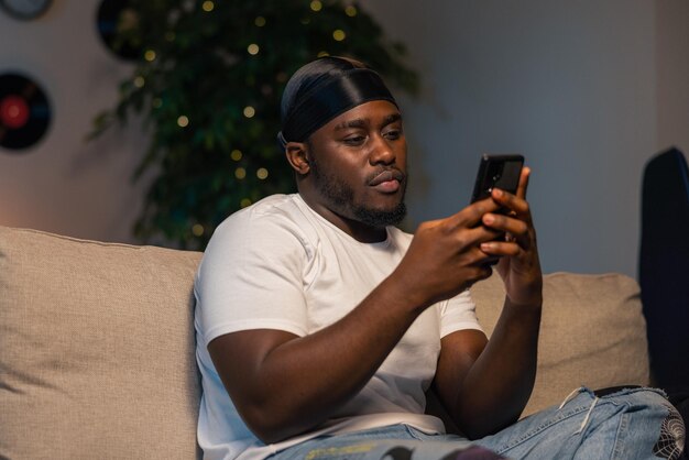 Feliz hombre de negocios barbudo usando el teléfono mientras se sienta en el sofá en el concepto de hogar moderno de los jóvenes