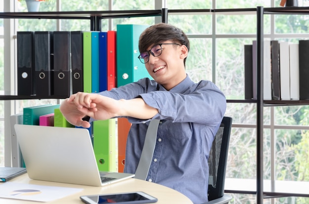 Feliz hombre de negocios en camisa azul estirando los brazos para deshacerse del dolor muscular aliviar la tensión en la oficina