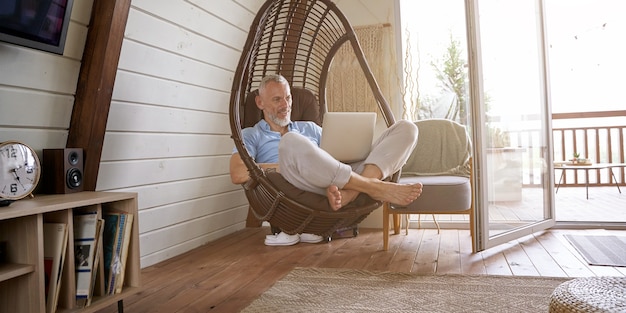 Feliz hombre de negocios caucásico de mediana edad en ropa casual sentado en una silla de columpio en su moderno