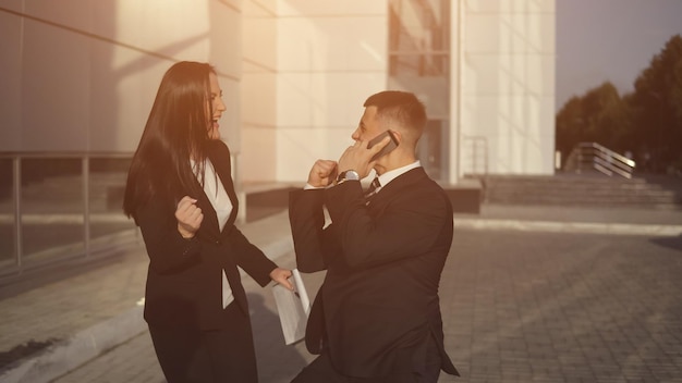 Feliz hombre de negocios está hablando por teléfono inteligente junto a la mujer asistente joven positiva en el fondo del centro de negocios. luz de sol