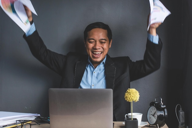 Feliz hombre de negocios exitoso sonriendo mira la computadora portátil mientras levanta ambas manos y sostiene el autobús