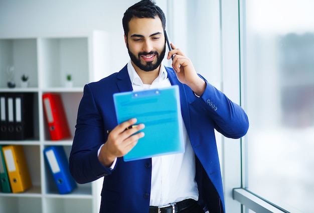 Feliz hombre de negocios hablando por teléfono móvil y sosteniendo en brazos portátil