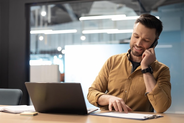 Feliz hombre de negocios hablando por teléfono trabajando en una laptop en la oficina