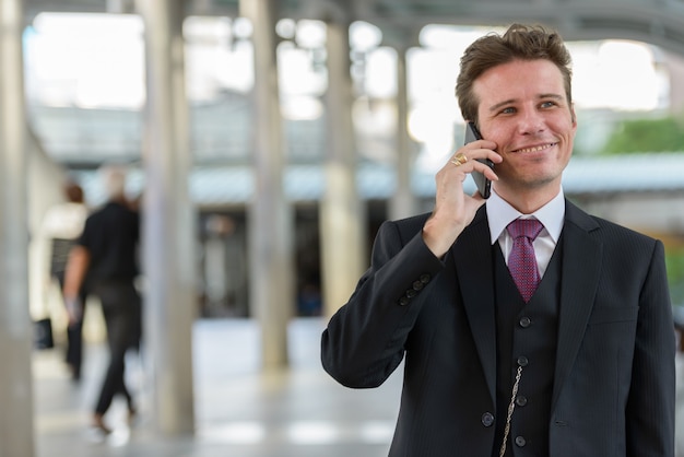 Feliz hombre de negocios pensativo sonriendo y hablando por teléfono móvil