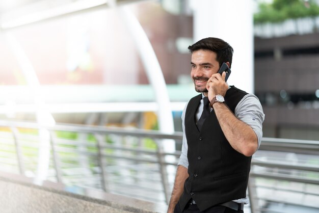 Feliz hombre de negocios de pie al aire libre llamando por teléfono móvil en la ciudad