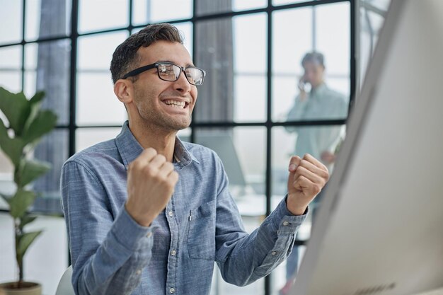 Feliz hombre de negocios regocijándose por el éxito en el lugar de trabajo en la oficina mirando la pantalla del portátil con expresión eufórica