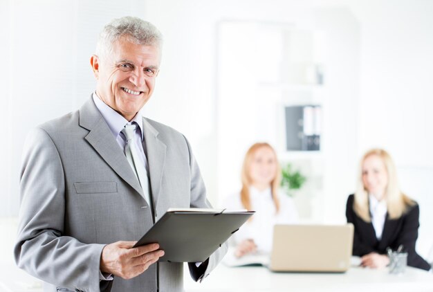 Feliz hombre de negocios senior con documentos en la oficina. Mirando a la cámara. Enfoque selectivo.