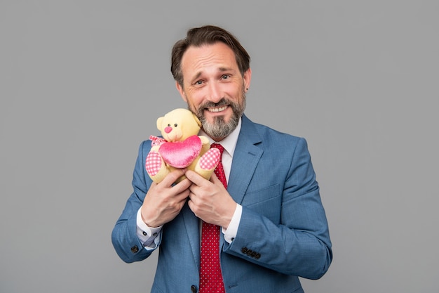 Feliz hombre de negocios senior en traje mantenga oso de juguete sobre fondo gris, día de San Valentín.