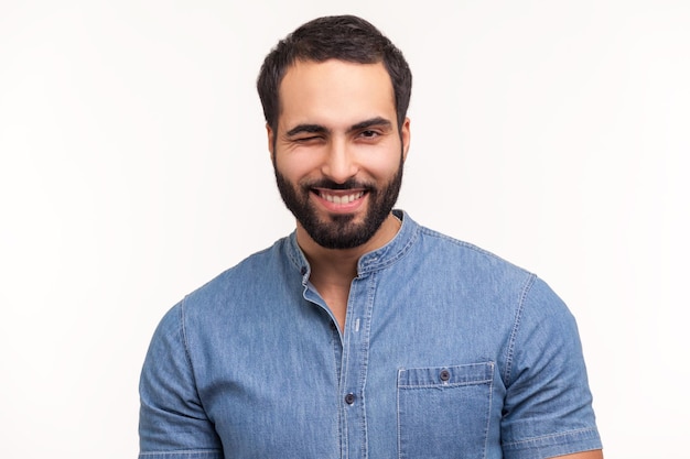 Foto feliz hombre positivo con barba guiñando un ojo mirando a la cámara con una sonrisa juguetona coqueteando tiene buen humor esperando la fecha disparo de estudio interior aislado sobre fondo blanco