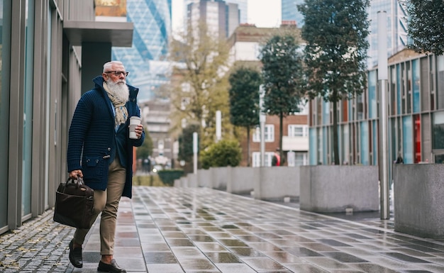 Feliz hombre senior de negocios caminando al trabajo en el día lluvioso de otoño Cara de enfoque