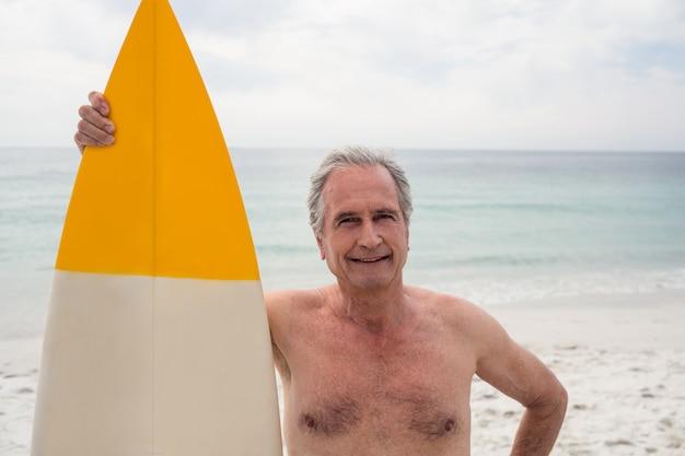 Feliz hombre senior de pie en la playa con tabla de surf