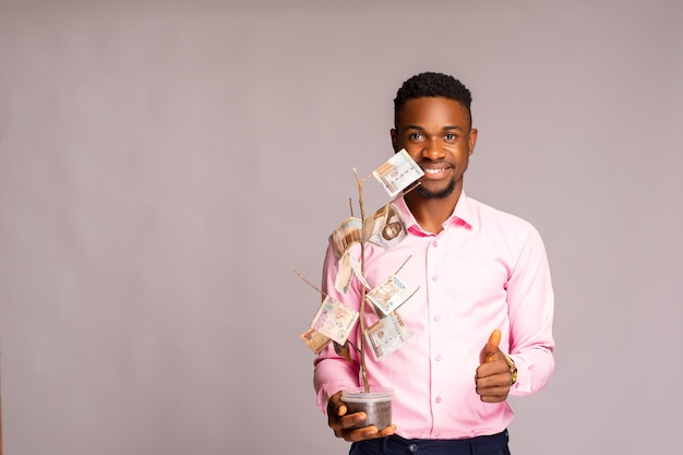 Feliz homem africano isolado sobre fundo branco sorrindo, ele segura uma árvore de investimento e fez os polegares para cima