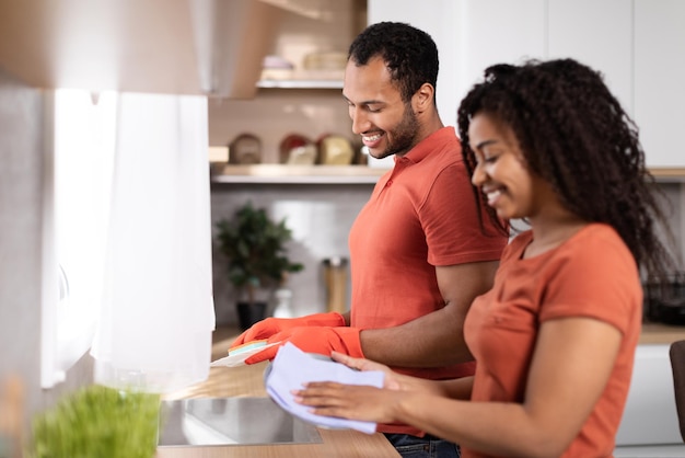 Feliz homem africano milenar e senhora nas mesmas camisetas lavando pratos aproveitam o tempo juntos