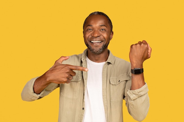 Feliz homem afro-americano de meia-idade em show casual de dedo no smartwatch com tela em branco