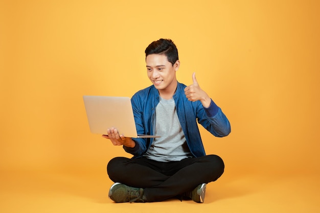 Feliz homem asiático animado segurando laptop e levantando o braço para comemorar sucesso ou conquista