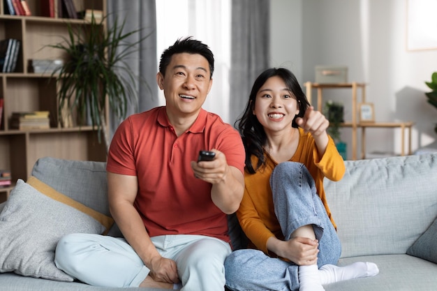 Feliz homem asiático e mulher assistindo TV em casa