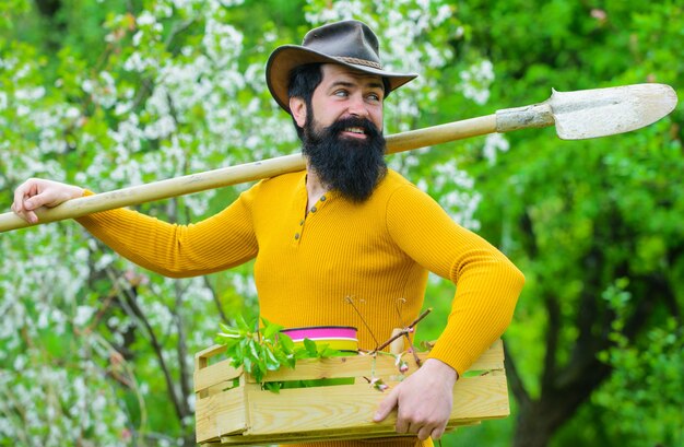 Feliz homem barbudo com ferramentas de jardinagem no jardim.