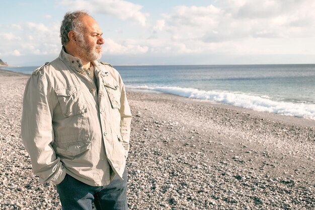 Foto feliz homem barbudo de meia-idade caminhando ao longo de uma praia de inverno deserta