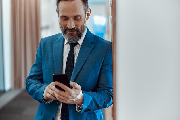 Feliz homem barbudo digitando no celular no escritório